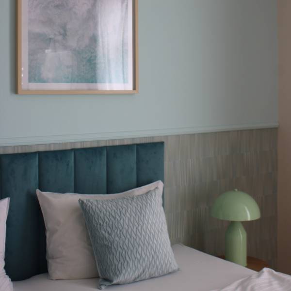 Teilansicht eines renovierten Hotelzimmers im Hotel Hüttmann mit modernem Design, gepolstertem Kopfteil und pastellgrüner Nachttischlampe