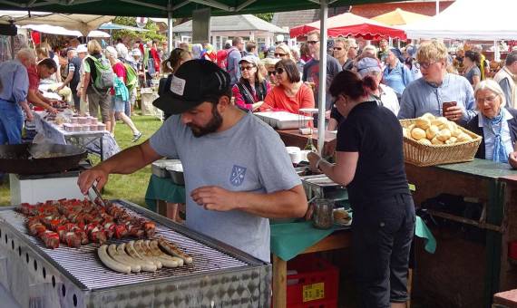 Grillstand auf einem gut besuchten Markt mit Fleischspießen, Bratwürsten und Menschen in der Warteschlange