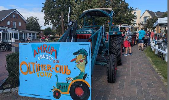 Ein Hanomag-Traktor mit bemaltem Schild „Amrum grüßt den Oldtimer-Club Föhr“ mit Besuchern.