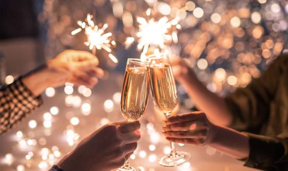 Vier Personen stoßen vor festlichem Hintergrund mit Sekt an und halten Wunderkerzen in der Hand