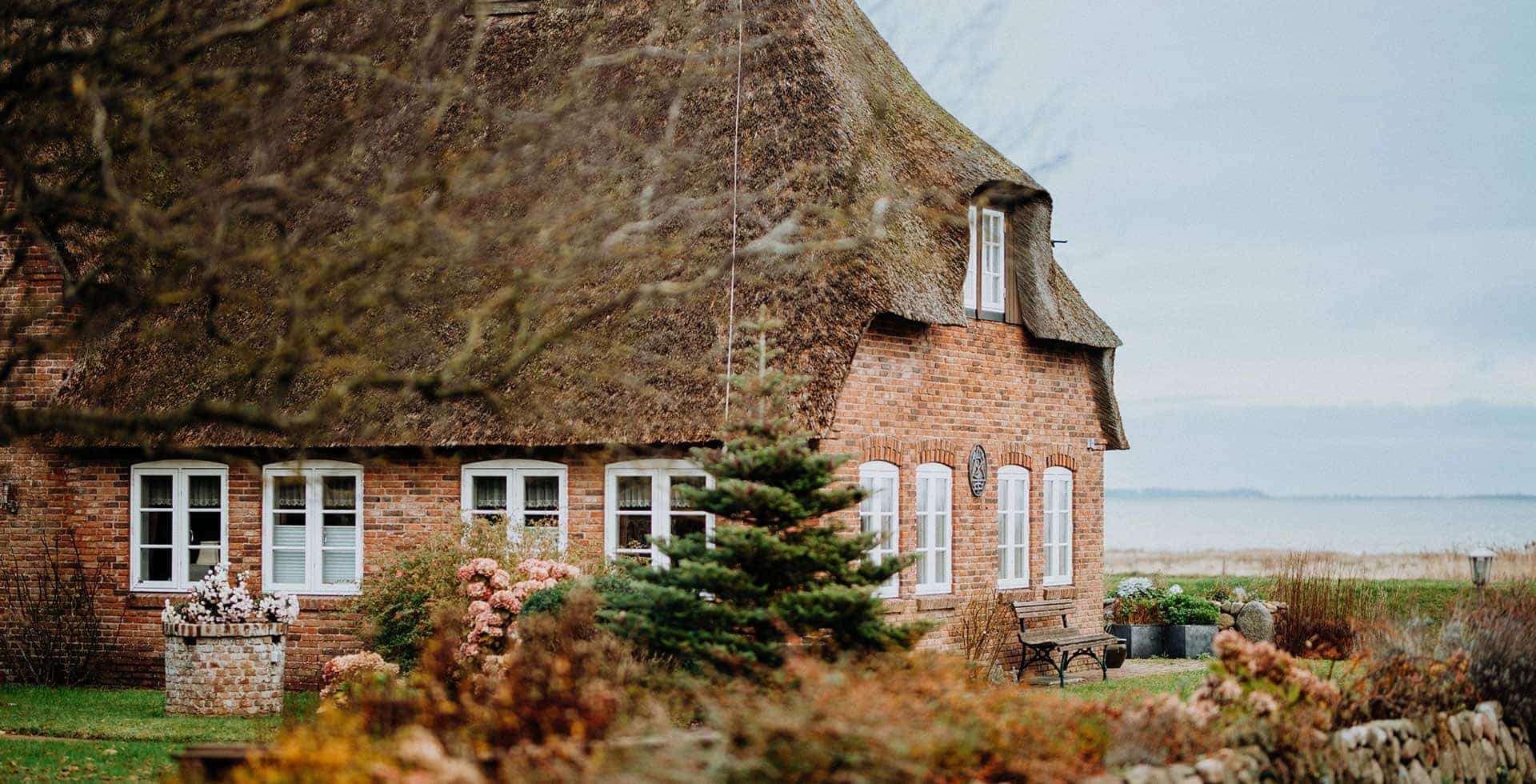 Klassisches Reetdachhaus aus roten Backsteinen und Blick aufs Meer.